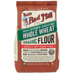 Organic whole wheat flour from Bob's Red Mill, shown in a clear bag with a scoop on a wooden surface.