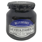 Jar of La Vieja Fabrica Blueberry Jam with fresh blueberries on a rustic wooden table.
