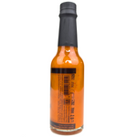 Bottle of The Serial Pickler Kimchi Hot Sauce with label visible, featuring spicy red chili and garlic ingredients, in a grocery setting.
