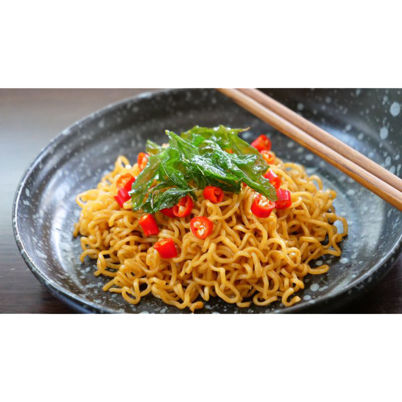A bowl of Domin Mie Spicy Thai Basil Chicken instant noodles with chopped basil and chili peppers on top.