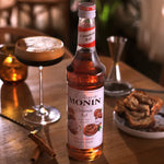 Bottle of MONIN Cinnamon Syrup 700ml for drinks and desserts, featuring a clear label and cinnamon flavor branding.
