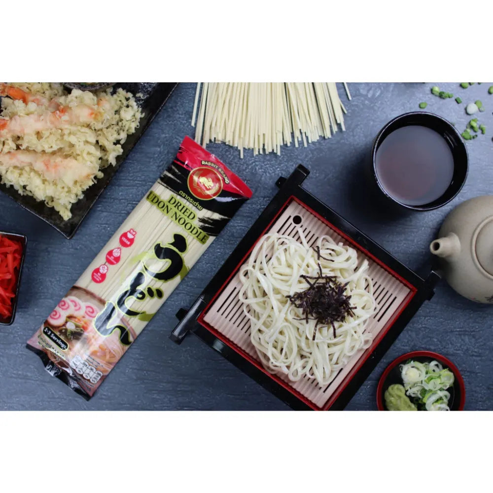 Dry Rabbit Brand Udon Noodles in a clear plastic bag, ready for cooking, with thick, white wheat noodles visible.