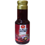 Jadjans Nam Jim Jaew spicy Thai dipping sauce in a glass bottle with fresh herbs and chili peppers around it.